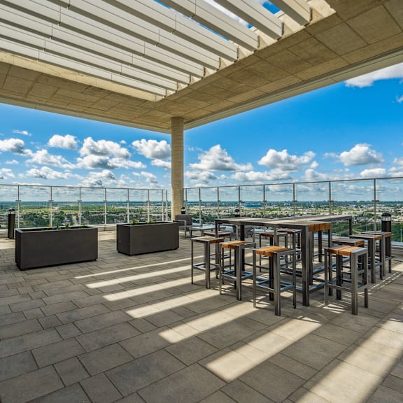 a rooftop patio with a bar and chairs overlooking a cityscape.