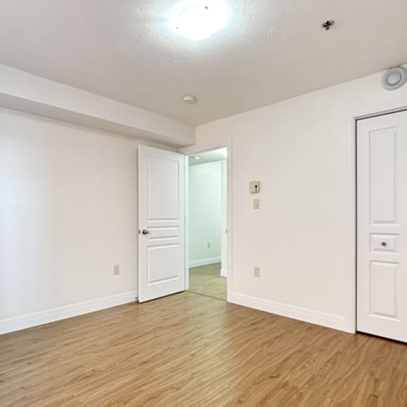 a room with white walls and wooden flooring, featuring a door and a window.