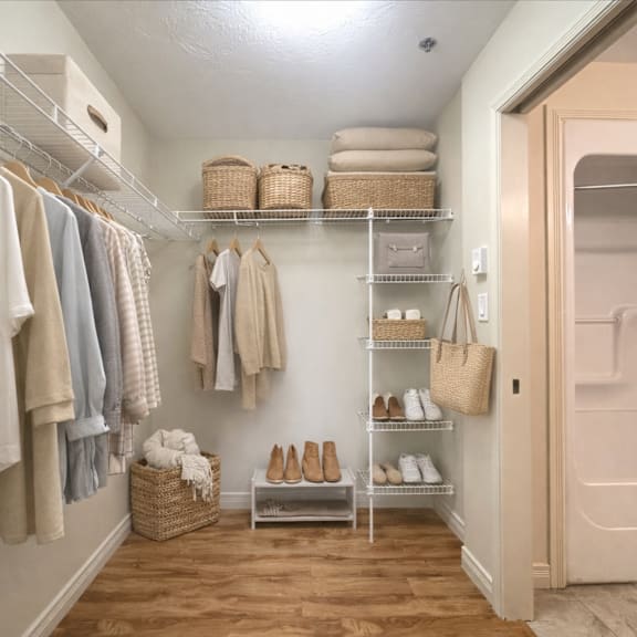 a hallway with a white wall and a white door with a shelf and clothes hanging.