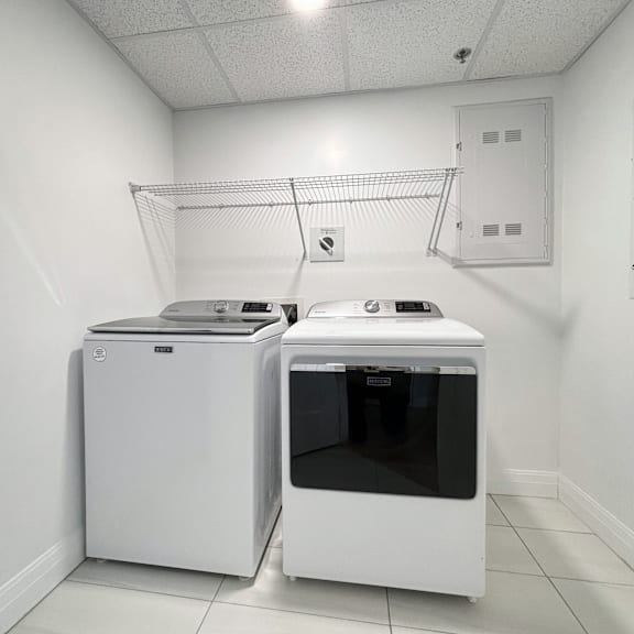 a white dishwasher and dryer in a clean, white-walled laundry room.