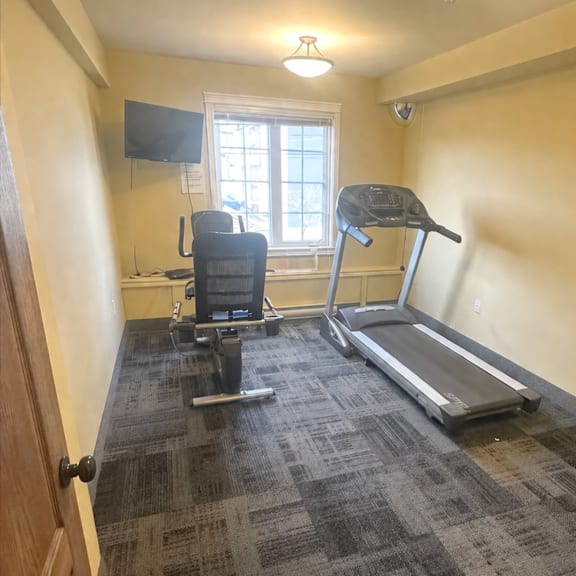 a room with a treadmill, a chair, and a television.