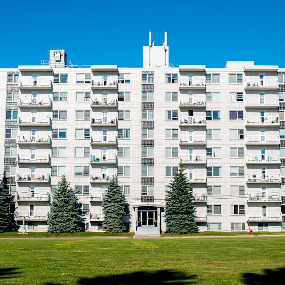 a large white apartment building with balconies and trees in front.