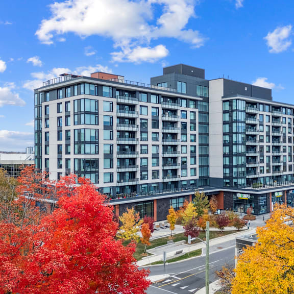a modern multi-story building with balconies and a parking lot in front.