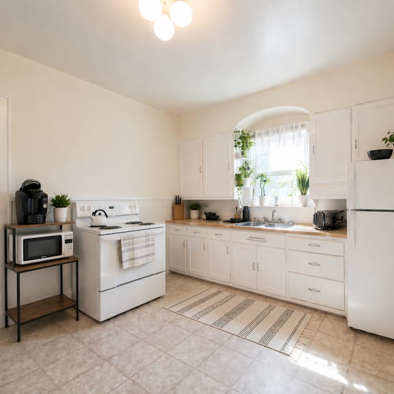 a white kitchen with a microwave on a stand.