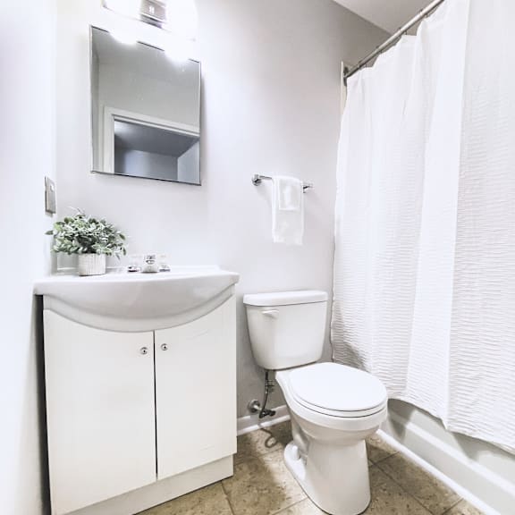 a white bathroom with a toilet, sink, and shower curtain.