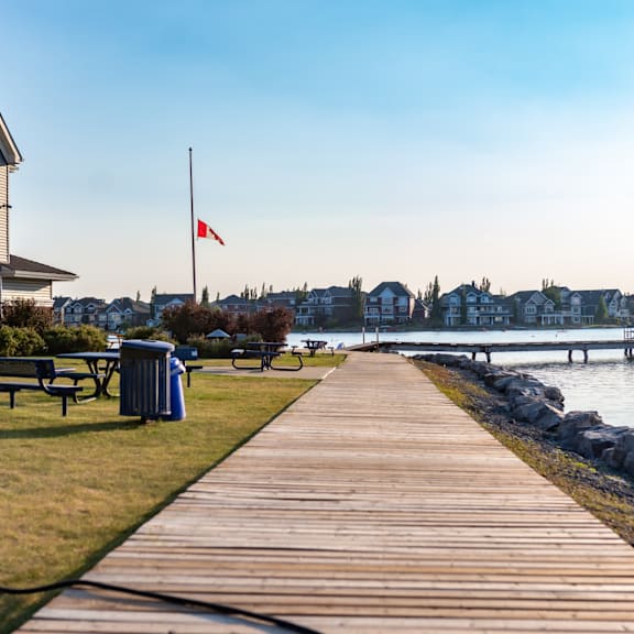 a wooden walkway leads to a body of water with a canadian flag in the background.