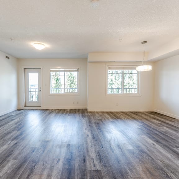 a spacious room with wooden floors and two windows.