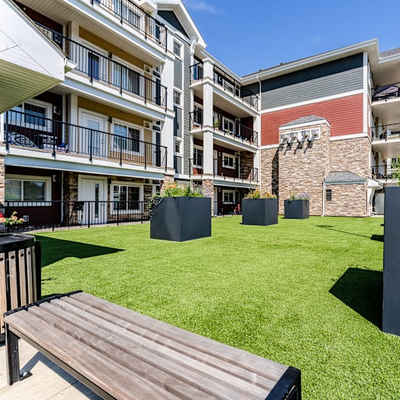 a wooden bench sits in the middle of a grassy area in front of a building.