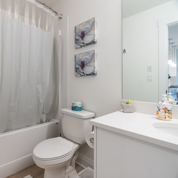 a white bathroom with a toilet, sink, and shower curtain.