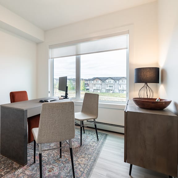a room with a desk, chairs, and a window overlooking a residential area.