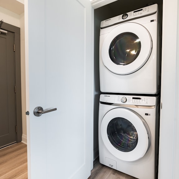 a white front load washing machine is stacked on top of another in a small laundry room.