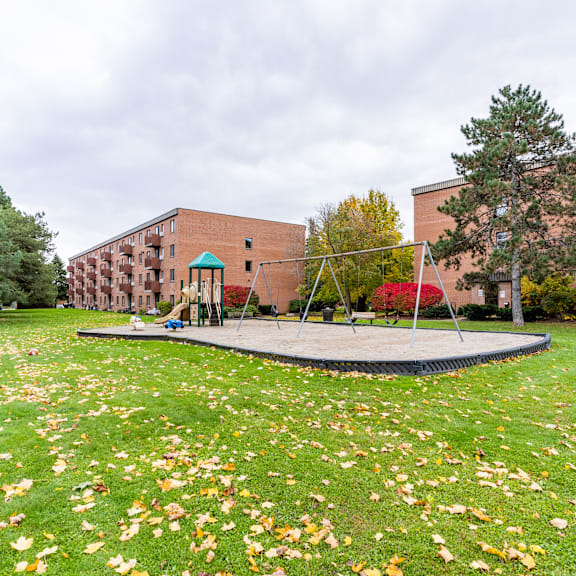 a playground with a trampoline and a slide in front of a brick building.