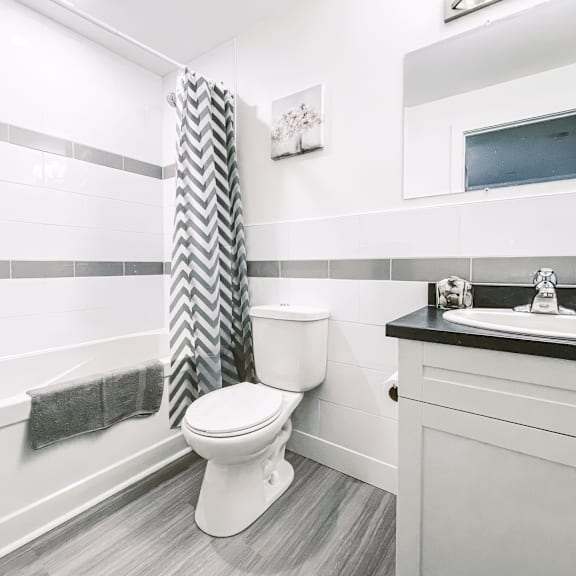 a white toilet in a bathroom with a grey and white shower curtain.