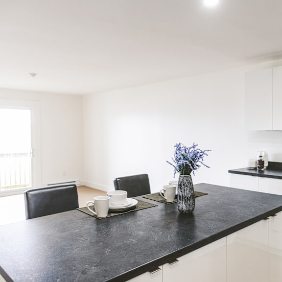 a black countertop with a vase of blue flowers and two cups on it.
