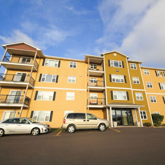 two cars parked in front of a yellow apartment building.
