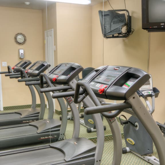 a gym with treadmills and a television mounted on the wall.
