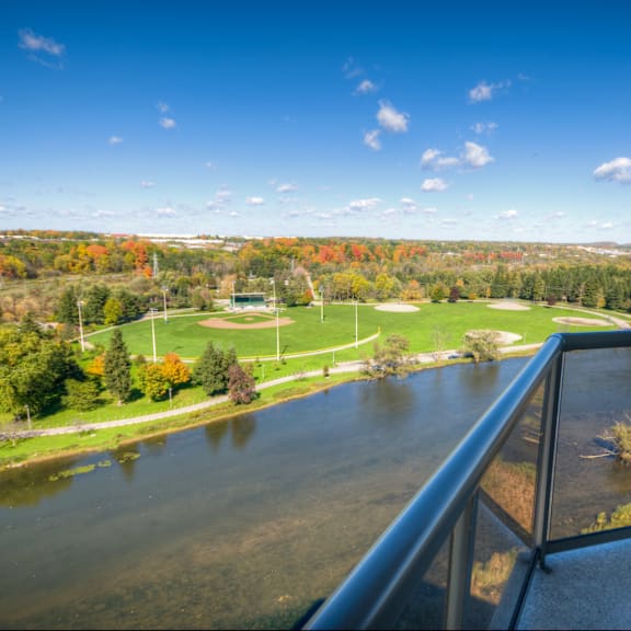 a view from a balcony overlooking a river, a baseball field, and a forest.