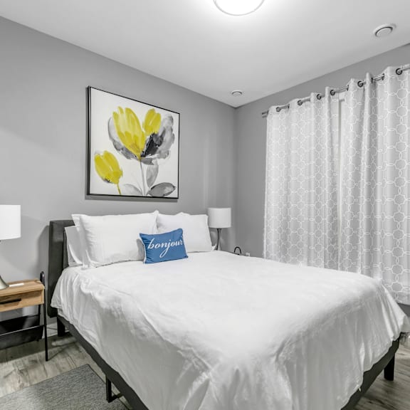 a bedroom with a large bed, a nightstand with a lamp, and a framed picture of yellow flowers on the wall.