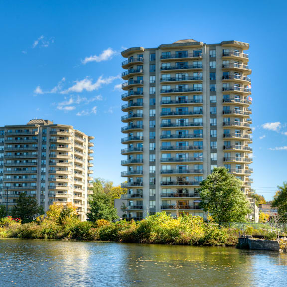 two tall residential buildings are situated next to a body of water.