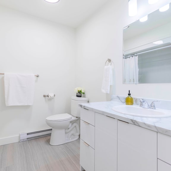 a white bathroom with a toilet, sink, and mirror.