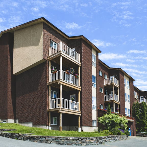 a large brick building with balconies and a stone wall in front.