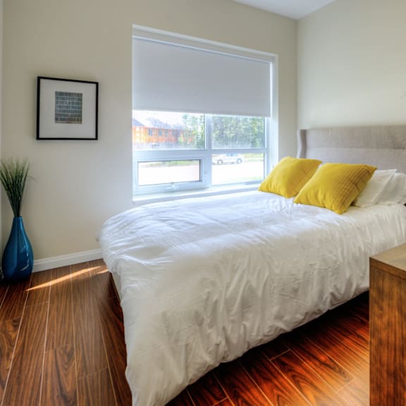 a bedroom with a bed, wooden nightstand, and a window with blinds.