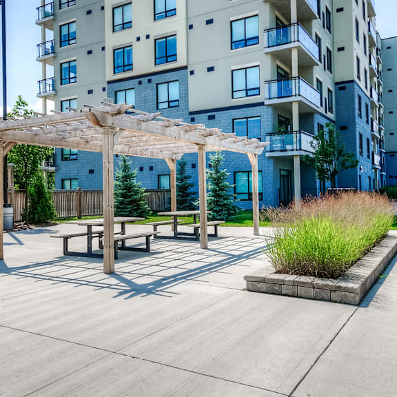 a patio area with a table and benches under a pergola in front of a building.