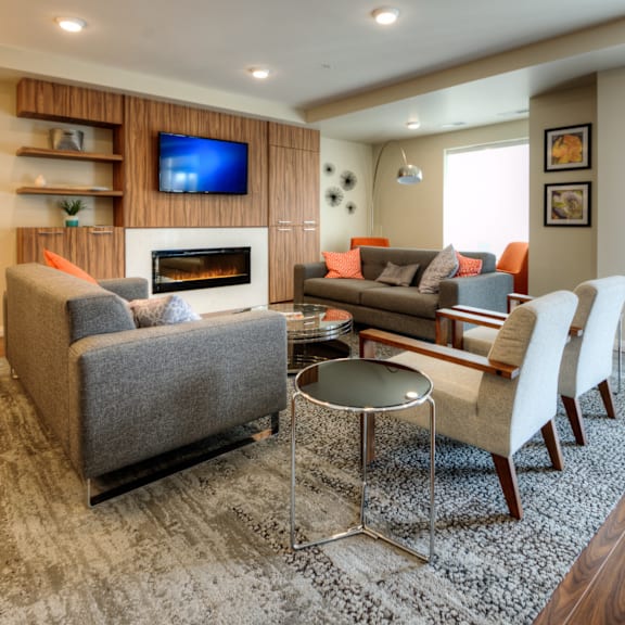 a living room with a grey couch, a grey armchair, a grey coffee table, a white chair, a fireplace, and a television on the wall.