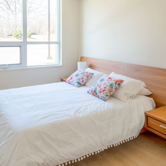 a bed with white sheets and floral pillows in a room with a large window.