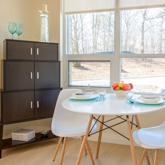 a dining room with a white table and chairs, a cabinet, and a view of trees outside the window.
