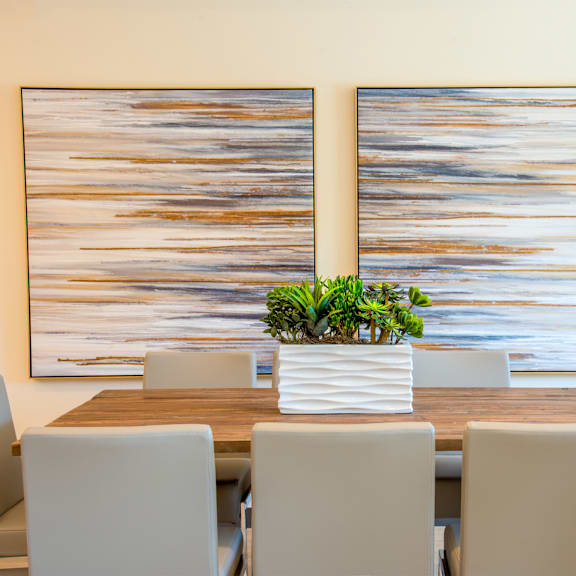 a table with chairs and a plant on it in front of two paintings.