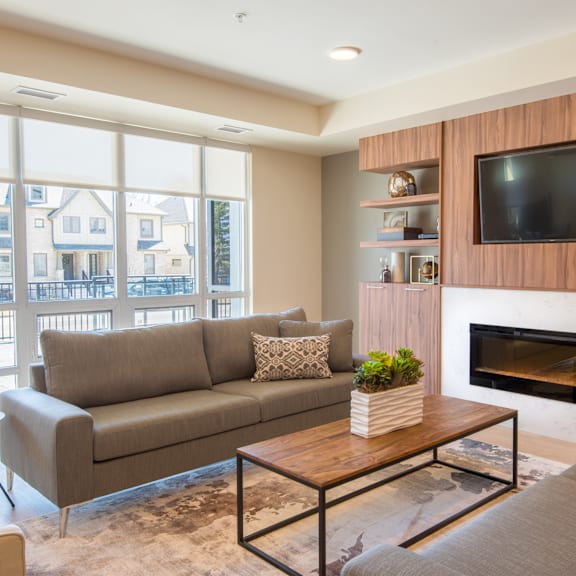 a living room with a grey couch, a wooden coffee table, a flat screen tv and a fireplace.