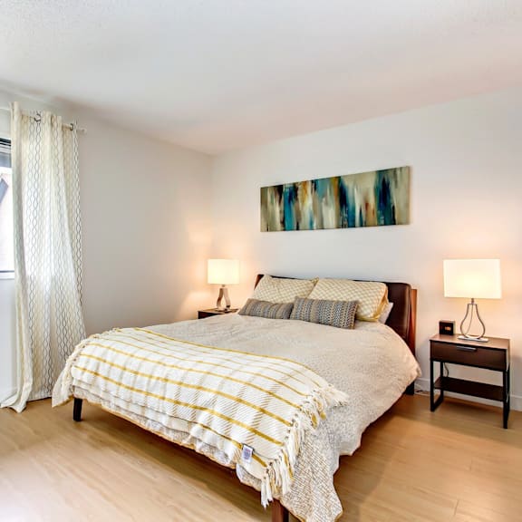 a bedroom with a bed, two lamps, and a painting on the wall.