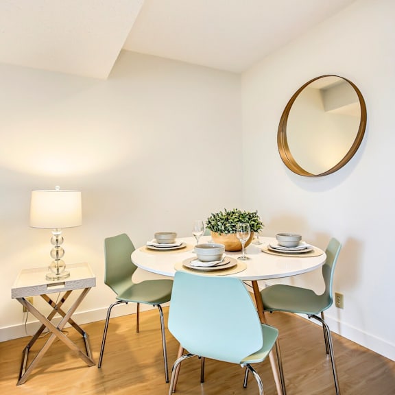 a white dining table with four chairs and a small plant on it.