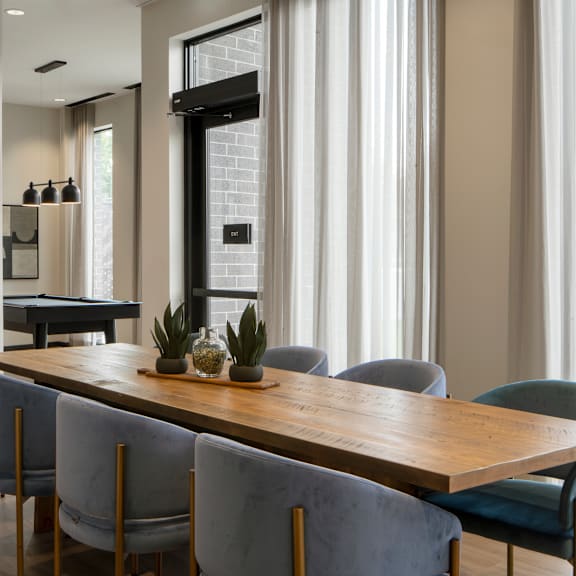 a long wooden table with grey chairs in front of a window.