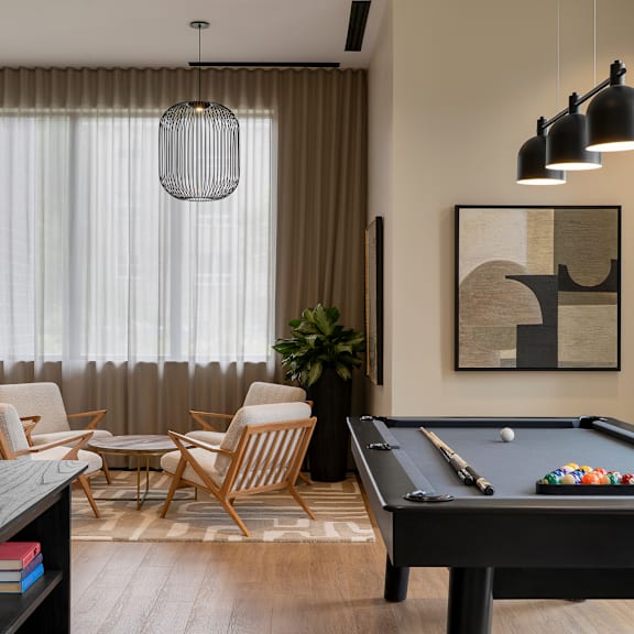 a pool table is in the middle of a room with a chair and a plant.