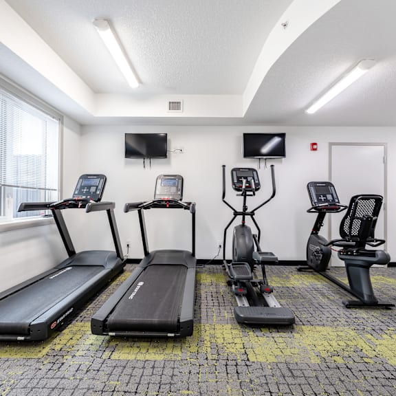 a gym with treadmills, exercise bikes, and a television.