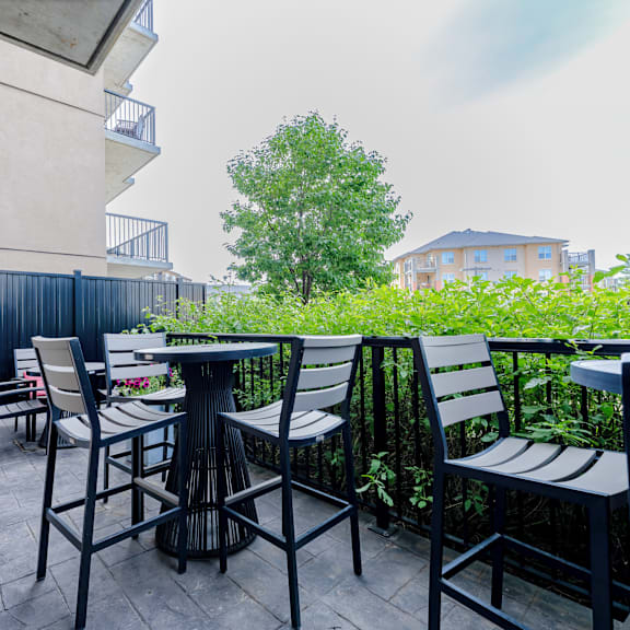a patio with a table and chairs surrounded by greenery.