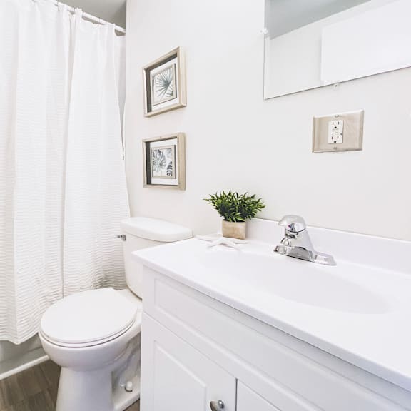 a white bathroom with a toilet, sink, and shower curtain.