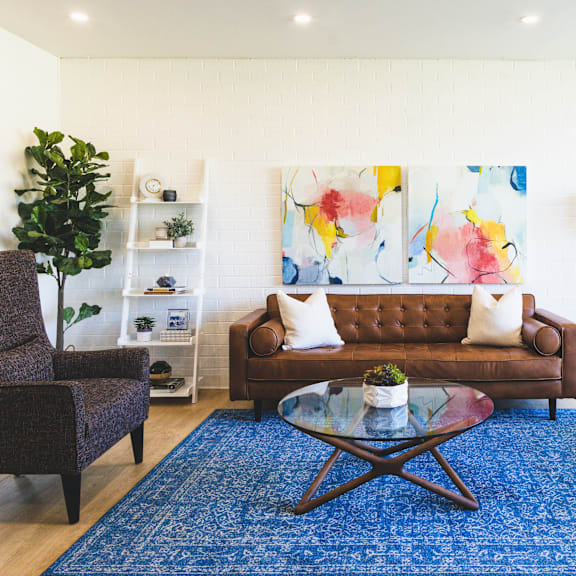 a living room with a brown couch, a brown chair, a glass coffee table and a blue rug.