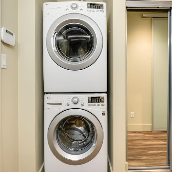 a white front load washing machine is stacked on top of another in a small room.