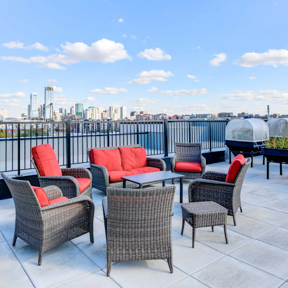 a patio with red cushions and grey wicker furniture overlooking a city skyline.