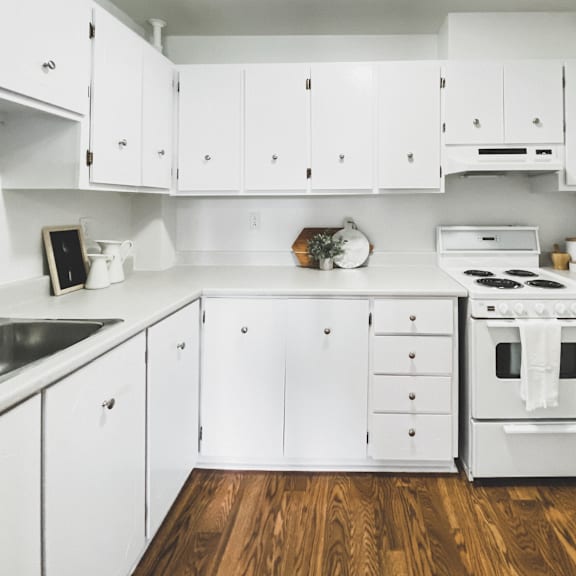 a white kitchen with wooden floors and a stove top oven.