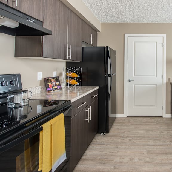 a black refrigerator stands in a kitchen with wooden cabinets and a white door.