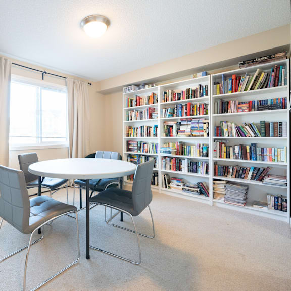 a room with a table, chairs, and a bookshelf filled with books.
