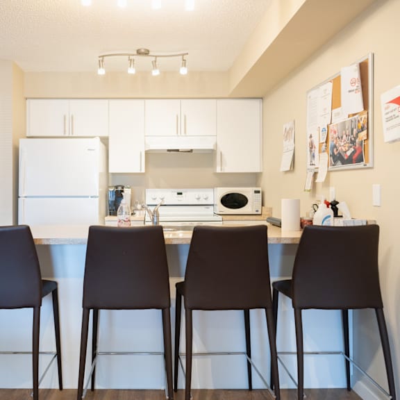 a kitchen with white appliances and brown chairs.