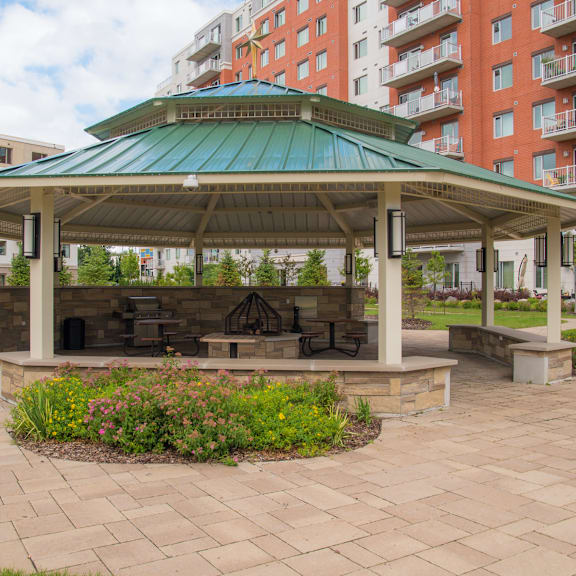 a gazebo with a green roof is surrounded by a brick patio and flowers.