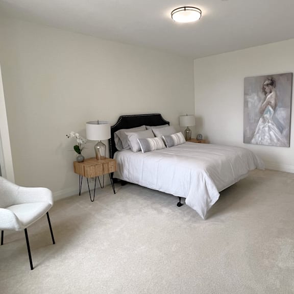 a white chair sits in a bedroom with a bed and a painting on the wall.