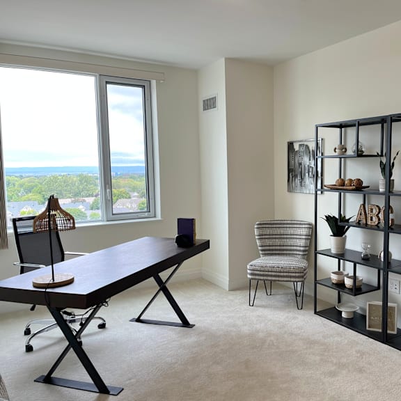 a black desk with a laptop and a chair in front of a window with a view of the ocean.