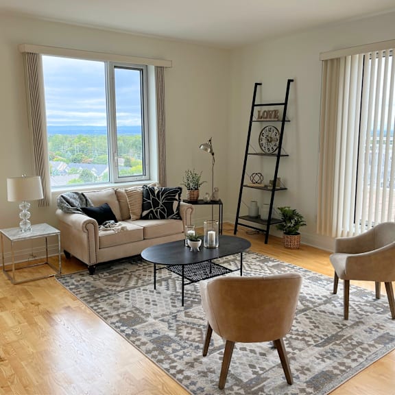a living room with a couch, two chairs, a table, and a large window with a view of the ocean.